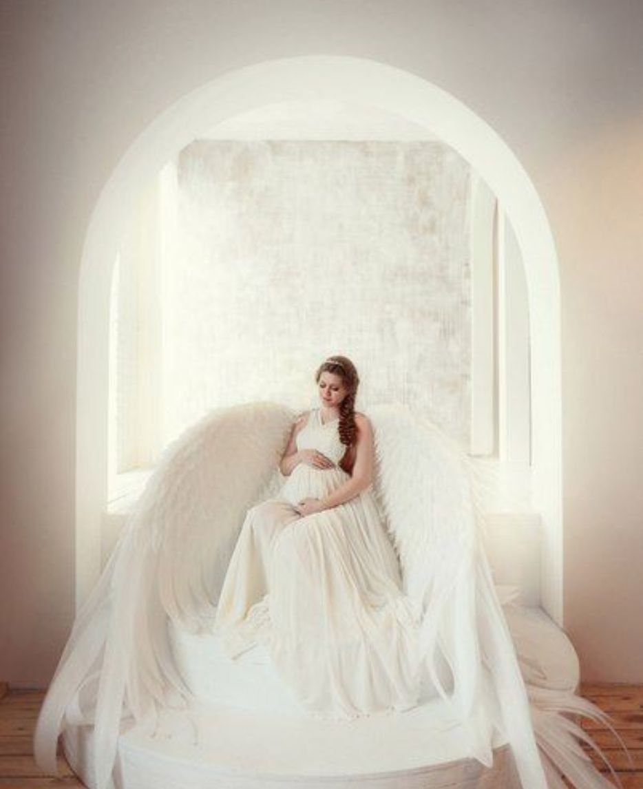 Elegant maternity photos with angelic wings, showcasing a glowing expectant mother in a serene and ethereal setting.