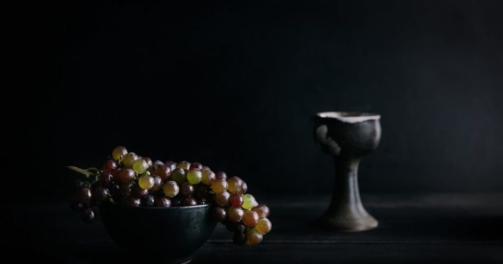 Still life photography setup featuring a camera on a tripod pointed at a table with arranged objects, including fruits, flowers, and a vase.