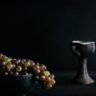 Still life photography setup featuring a camera on a tripod pointed at a table with arranged objects, including fruits, flowers, and a vase.