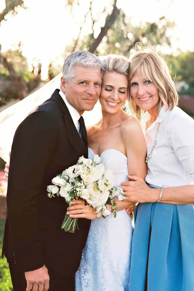 Bride smiling with her parents, enjoying a joyful moment at the wedding party.