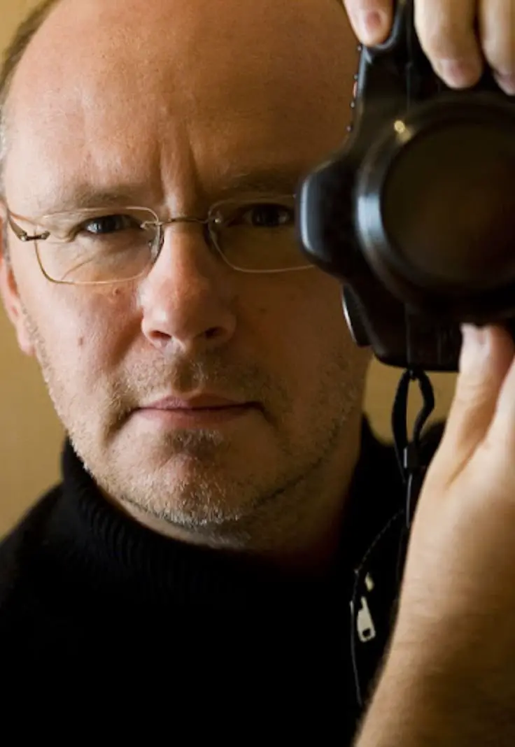 A man wearing glasses is holding a camera, ready to capture a moment.