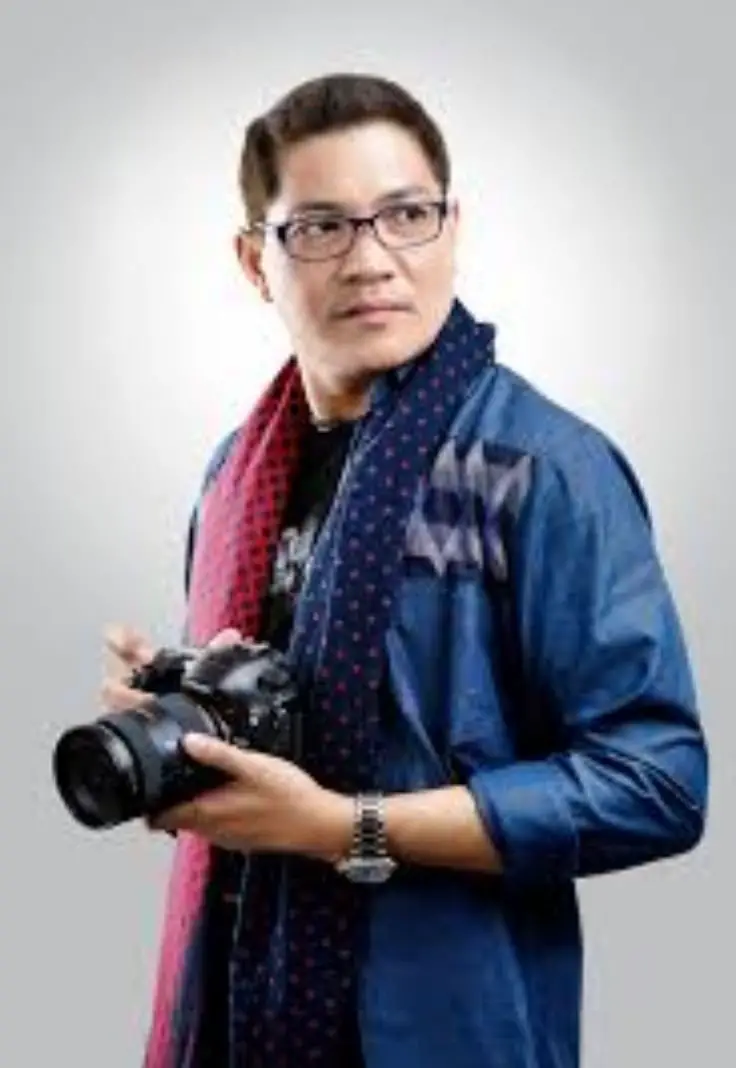 A man wearing glasses and a scarf is holding a camera, ready to capture a moment.