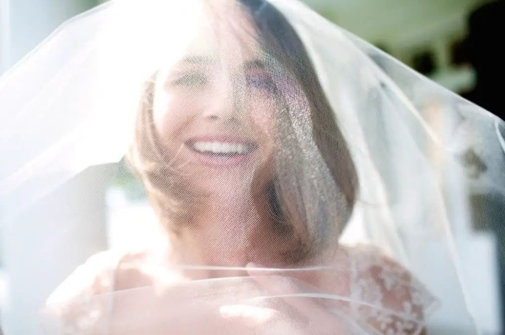 A joyful bride beams with happiness, her smile visible beneath the delicate fabric of her veil.