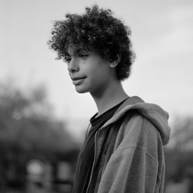 A black and white image of a young man with curly hair, showcasing his expressive features and thoughtful demeanor.