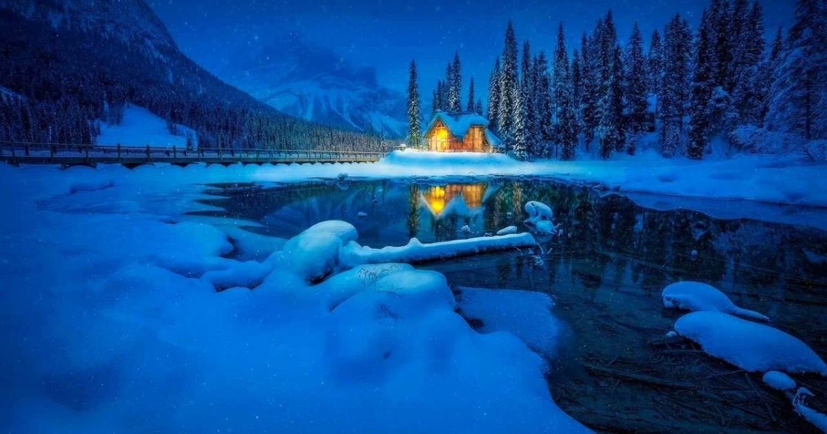 A cozy cabin illuminated by soft light, surrounded by a serene blanket of snow under a starry night sky.