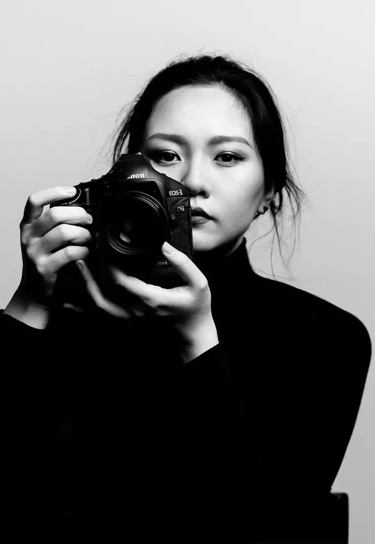 A woman holds a camera in front of her face, capturing a moment with a focused expression.