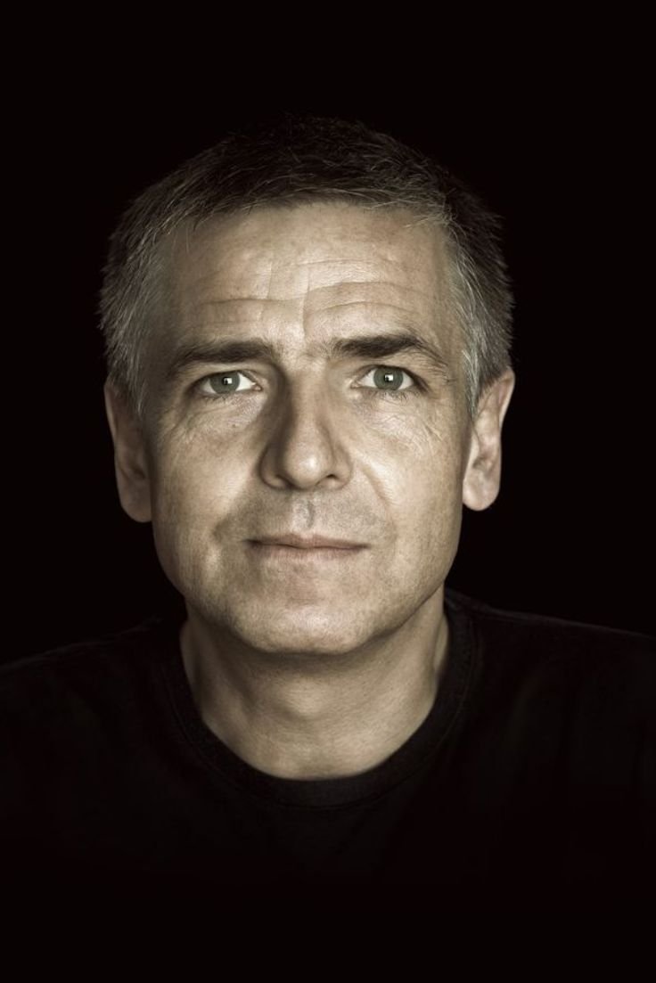 A man in a black shirt poses against a black background, showcasing contemporary photography's minimalist aesthetic.