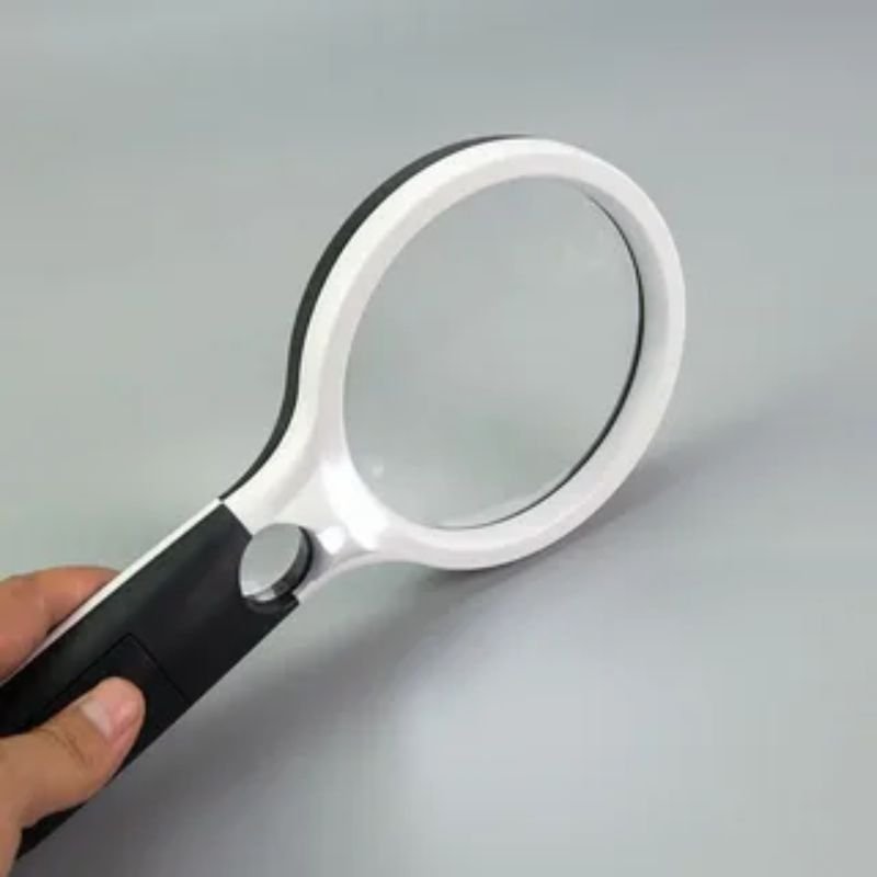 A person examines a white surface closely with a magnifying glass, showcasing creative photography techniques.