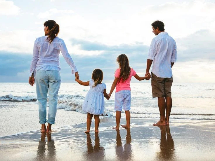  A family walks hand in hand on the beach at sunset, capturing a moment of unity and tranquility against a vibrant sky.