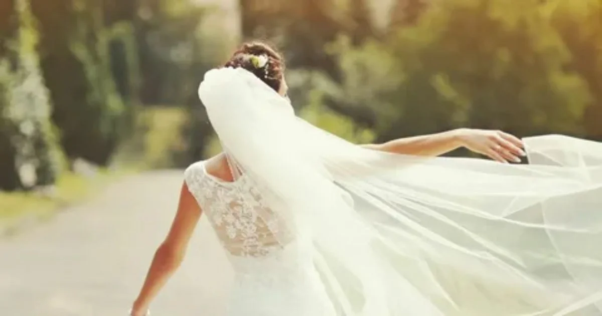 A bride walks down a road, her veil billowing in the wind, capturing a moment of elegance during wedding videography preparation.