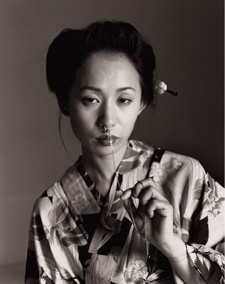 A woman in a colorful kimono gracefully holds a delicate flower, showcasing elegance and beauty.