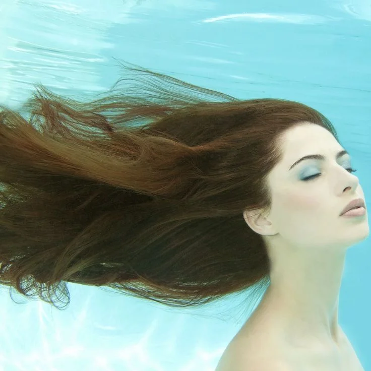 A woman with long hair gracefully swims underwater, embodying the enchanting essence of mermaid photography.