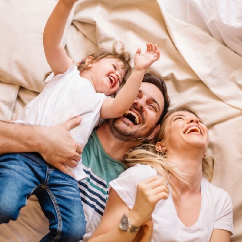 A happy family enjoying time on a bed, filled with laughter and smiles, complemented by playful photography props.