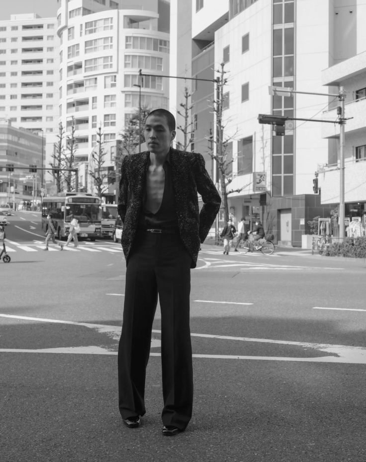 A man in a suit stands confidently on the street, surrounded by urban scenery.