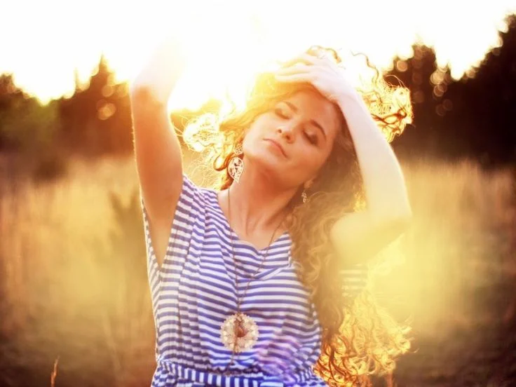 A woman in a striped dress stands gracefully in a field during a stunning sunset, capturing the beauty of the moment.