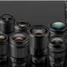 A collection of various camera lenses in different sizes arranged on a reflective black surface.