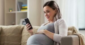 A pregnant woman at home, focused on her phone, reflecting the beauty and tranquility of her pregnancy experience.