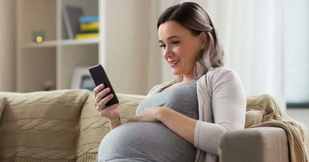 A pregnant woman at home, focused on her phone, reflecting the beauty and tranquility of her pregnancy experience.