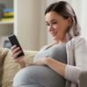 A pregnant woman at home, focused on her phone, reflecting the beauty and tranquility of her pregnancy experience.