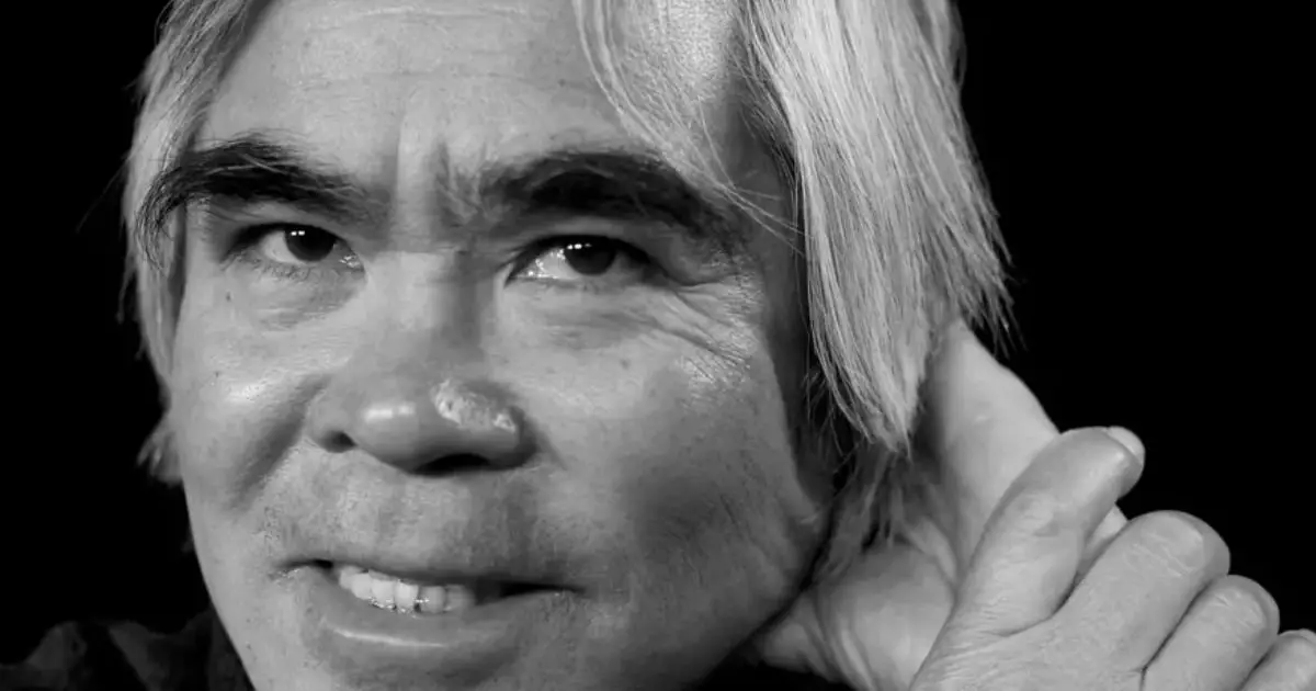 A man with striking white hair is featured against a dark backdrop, representing the impactful work of famous war photographers.