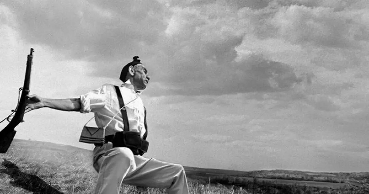 A man with a rifle stands on a hill, representing the legacy of famous war photographers in capturing history.