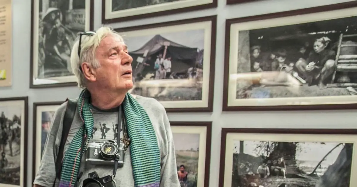 An older gentleman reflects on a wall displaying iconic photographs by celebrated war photographers.